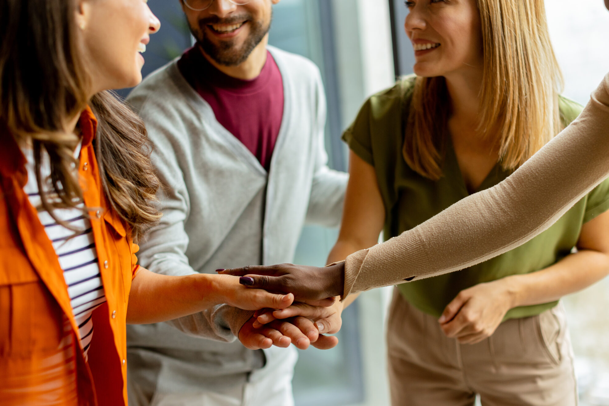Smiling colleagues stacking hands together to celebrate success through teamwork and collaboration.